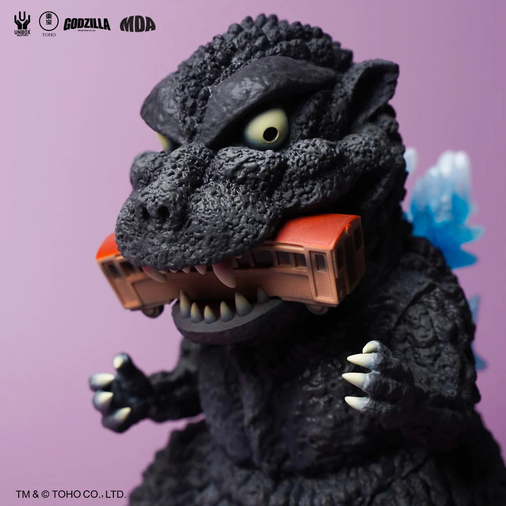 GODZILLA 1954 MDA PROJECT - Preorder figure, stylized chibi design, chomping an orange train, blue dorsal fins visible, logos in corner.