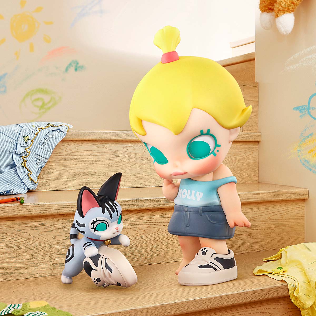 Baby Molly & Baby Tabby Series Figures on wooden steps, featuring a large-headed girl vinyl figure with a cat, crayons, and clothing scattered around.