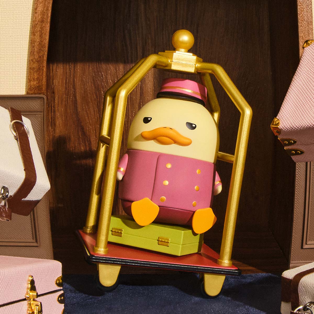The Grand DUCKOO Hotel Series Figures - Preorder: Duck figurine as bellhop on suitcase in brass luggage cart, part of a 12-design collectible series.