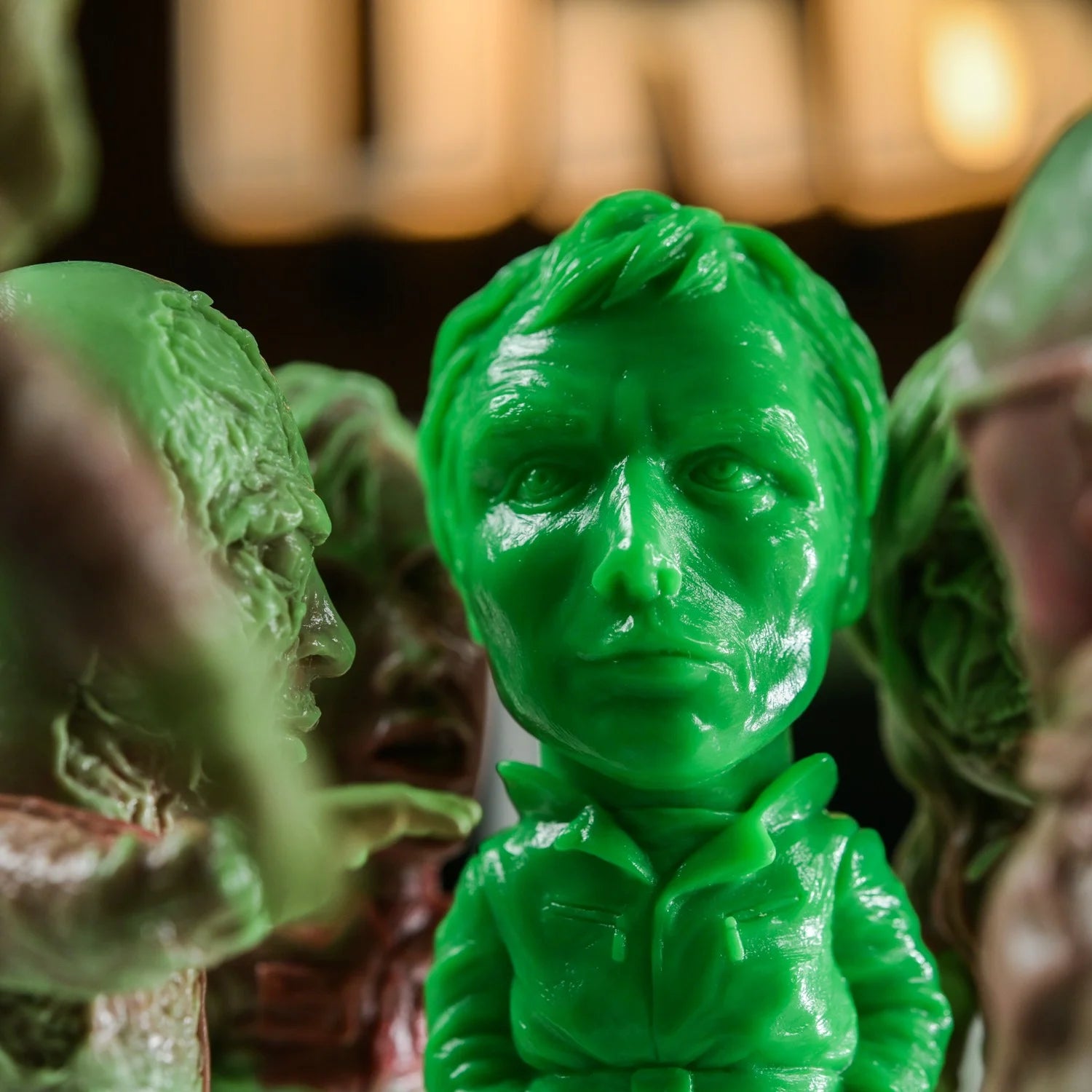 Bright-green bust from ZOMBI: DAWN OF THE DEAD Who Goes There Blind Box Series, showcasing detailed soft vinyl design by Naoki Okamoto, amidst muted figurines.