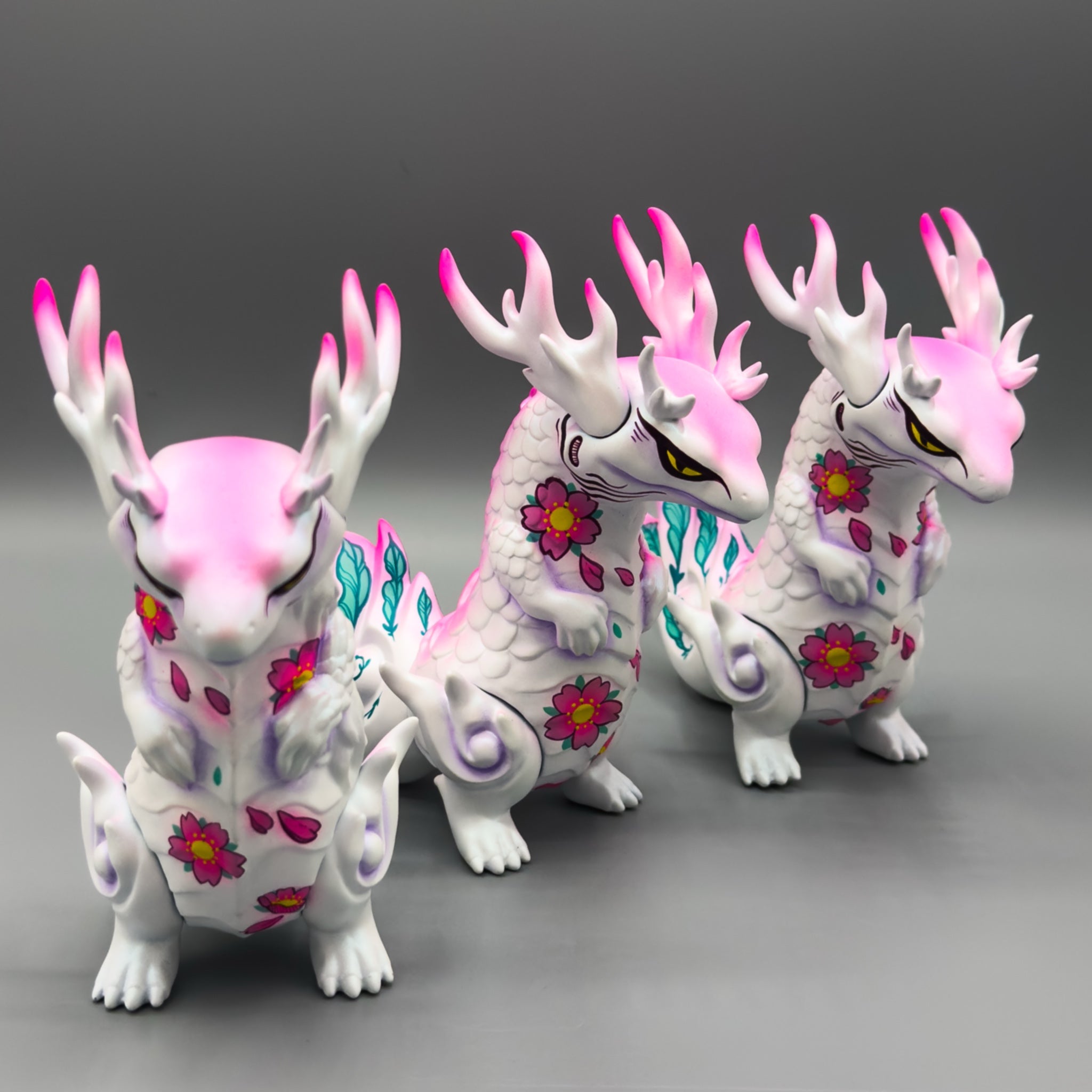 Celestial Abyss - Rinkaku Sakura by Tomodachi Island features three white dragon figurines with pink accents, cherry-blossom motifs, and teal tails, showcasing a whimsical art-toy design.