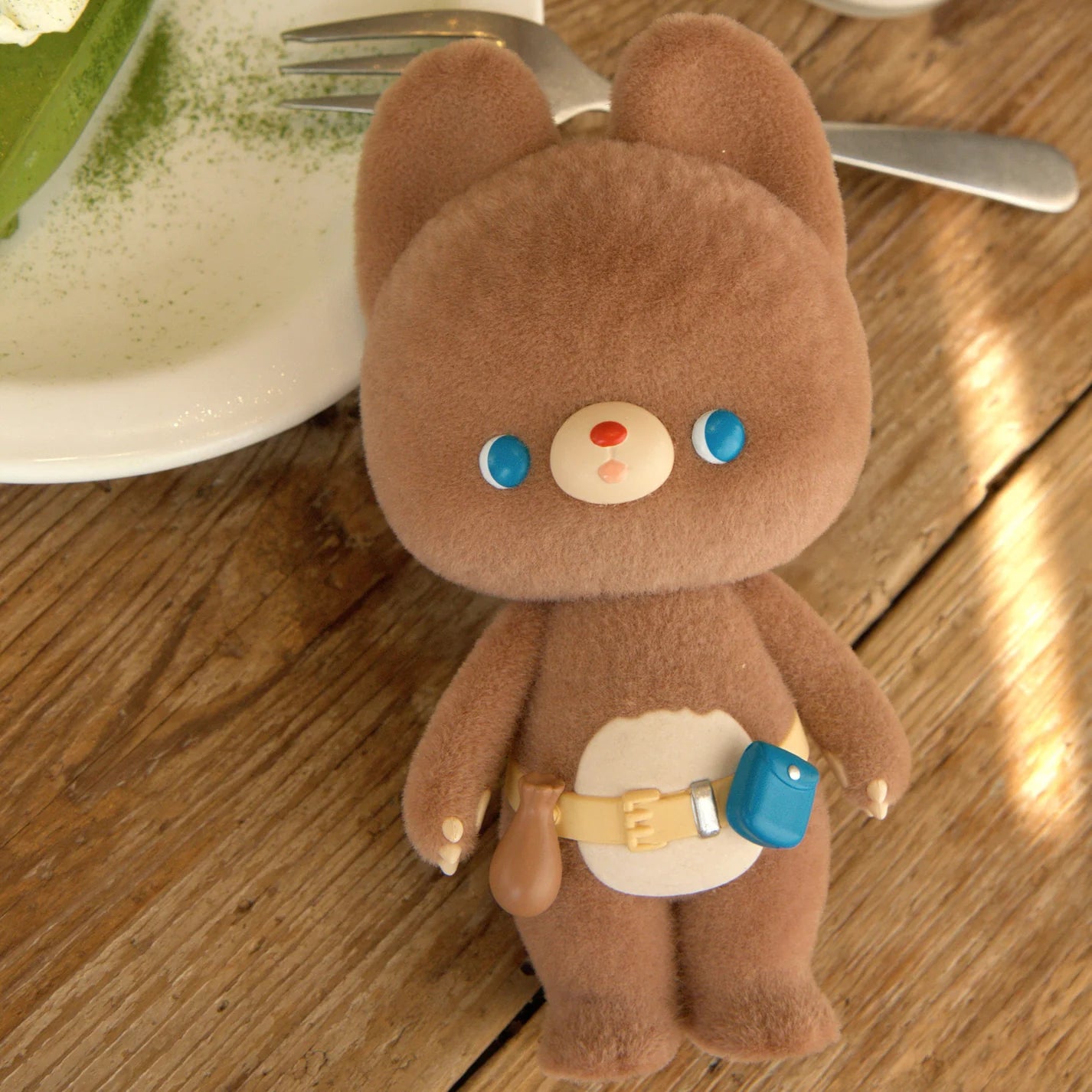 Kumaru the Forest Bear plush toy, shaped like a chubby bear with long ears, blue eyes, beige belly, wearing a belted pouch. Preorder.