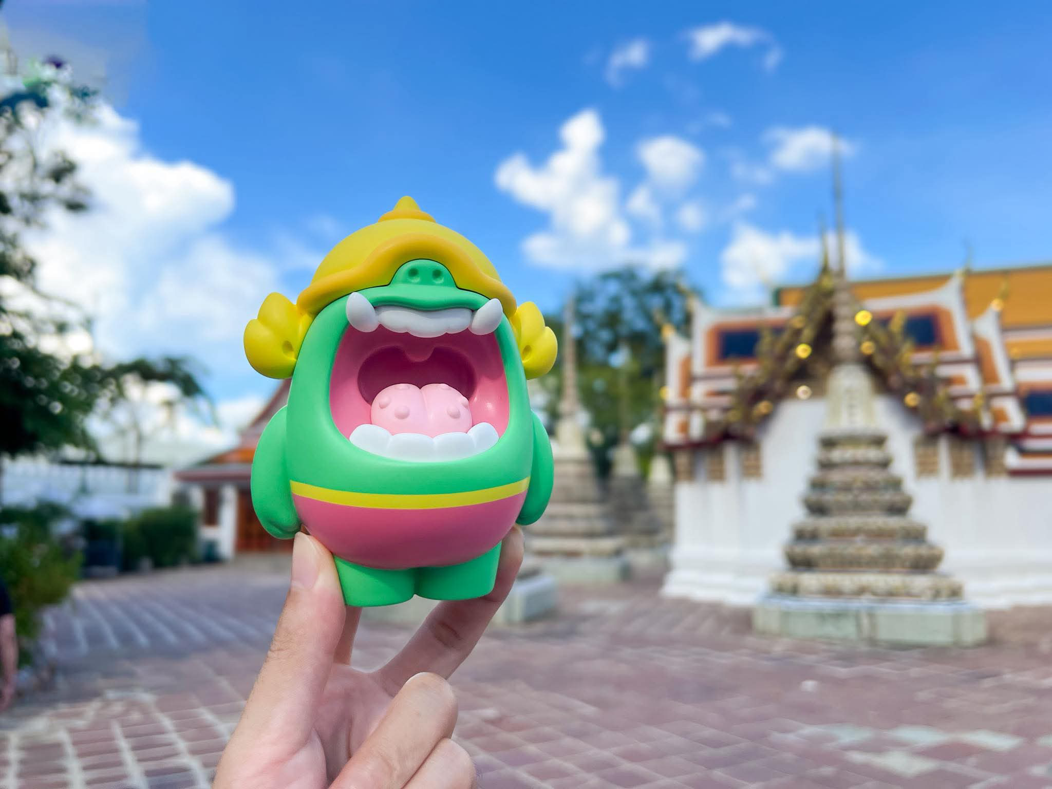 Mallow Yak by MUPA, a 12.5 cm green vinyl monster toy with tusks and helmet, held before an outdoor temple. Limited edition preorder.