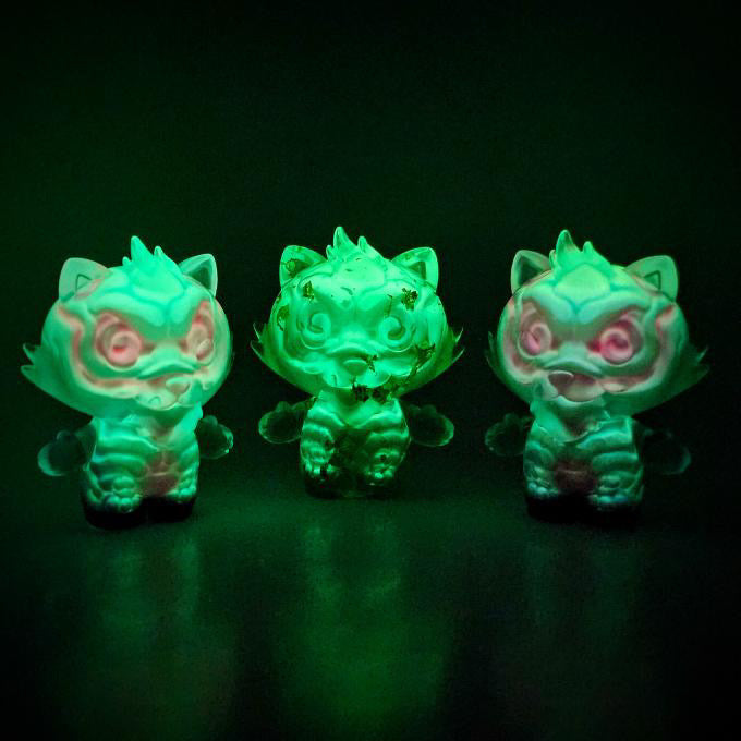 Three glow-in-the-dark, chibi-style Grandpa figurines by Motley Miscreations, resembling cartoonish animals, stand on a glossy surface, highlighting their fluorescent green glow.