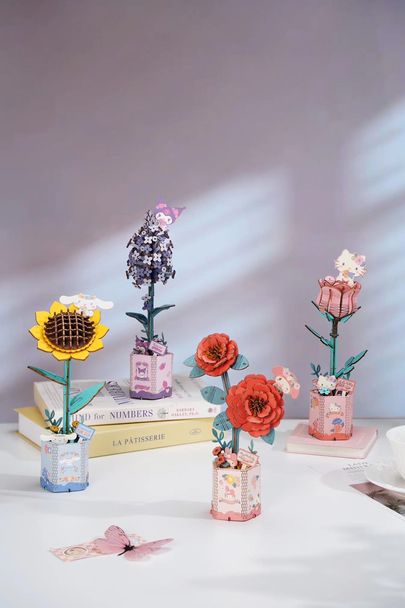 Hello Kitty Pink Rose 3D Wooden Puzzle Kit displayed with decorative paper flowers, books, and a teacup, offering a creative challenge and charming keepsake.