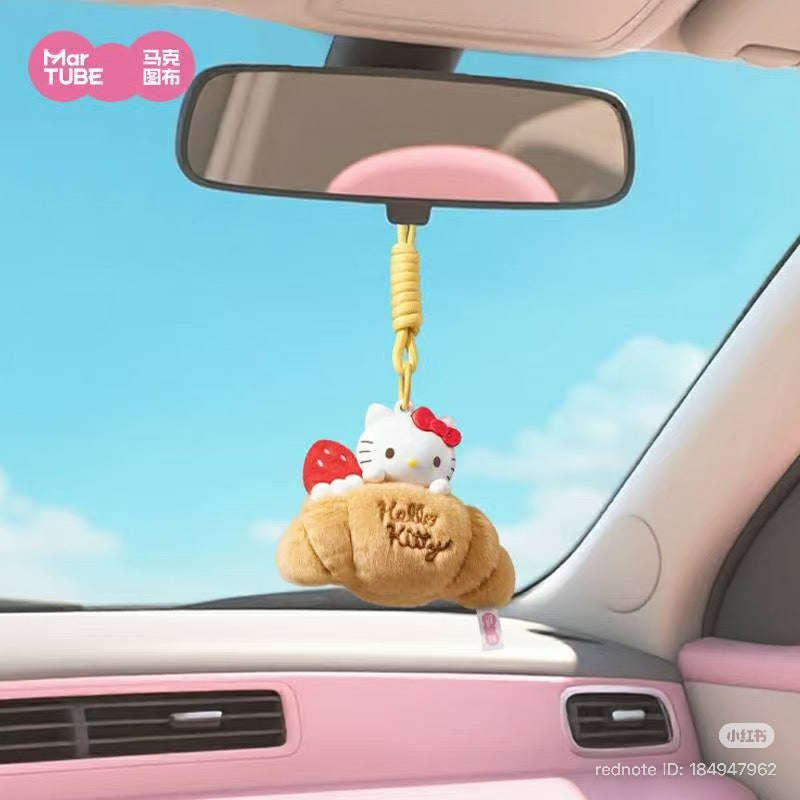 Hello Kitty Afternoon Tea Scented Blind Box Keychain featuring Kitty in a croissant, hanging from a car's light pink interior rear-view mirror.