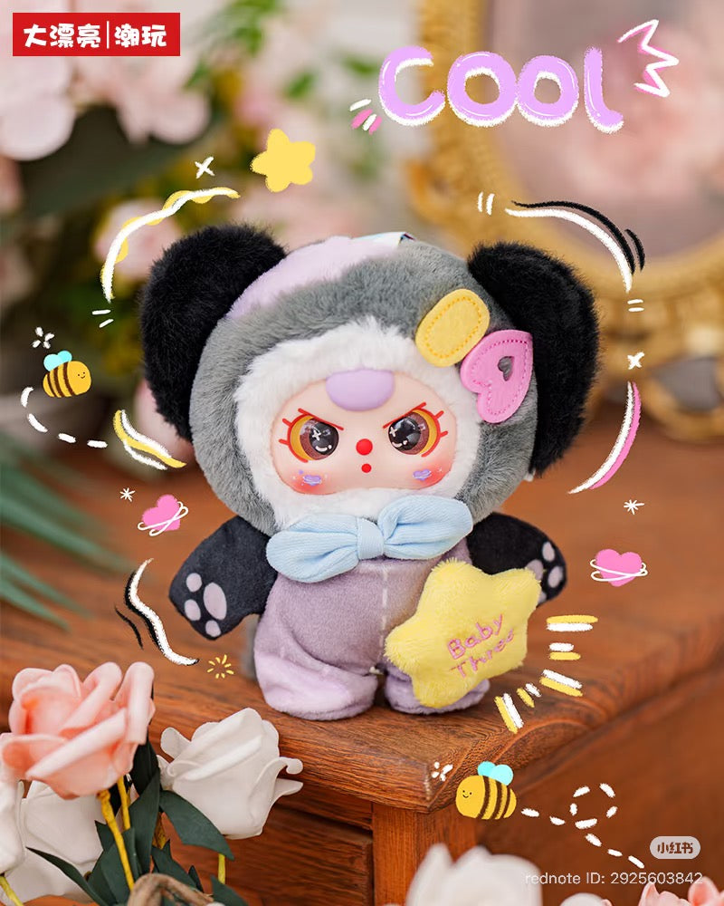 Baby Three - Sweet Dreams Plush Blind Box doll in animal onesie, holding a star, surrounded by doodles on a wooden surface with roses in the background.