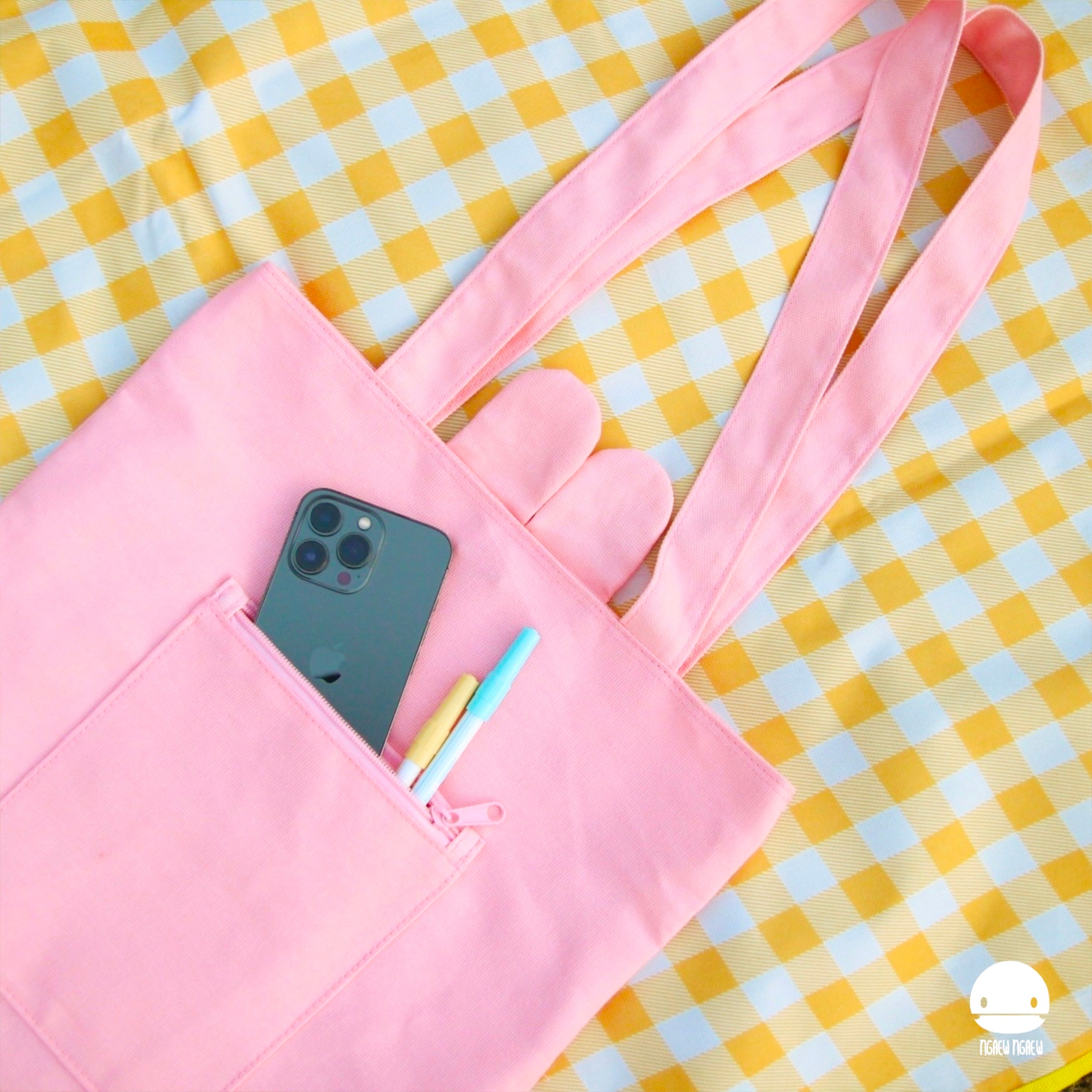 NGAEW NGAEW TOTE BAG on a checkered surface with a smartphone and markers in the front zip pocket, featuring long handles and a minimalist design.