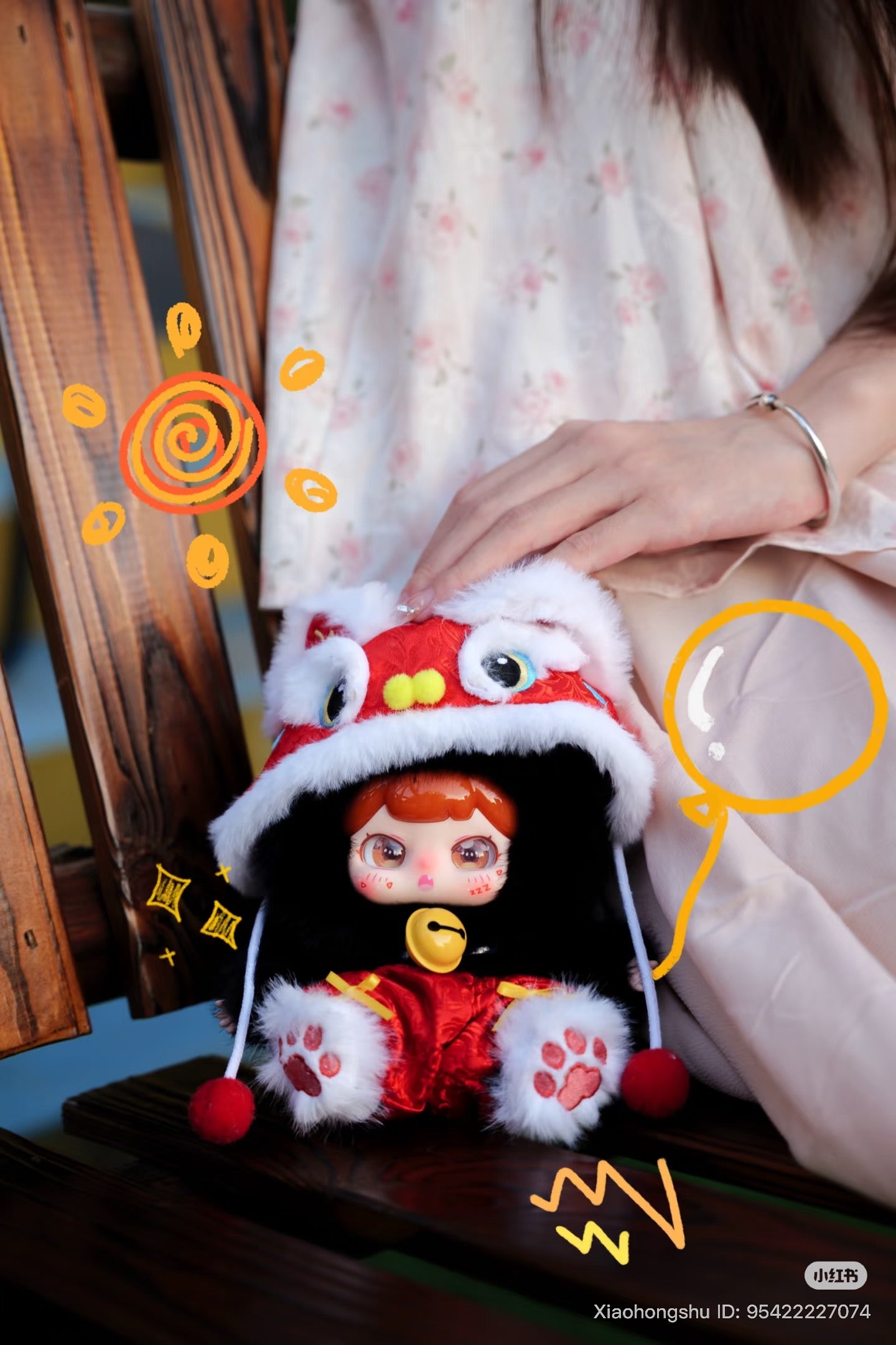 Baby Three - Xiaopaofu-Lucky Bell Plush Blind Box doll in red lion-dance outfit, sitting on a bench, with cartoon eyes, rosy cheeks, and pink paw-print feet.