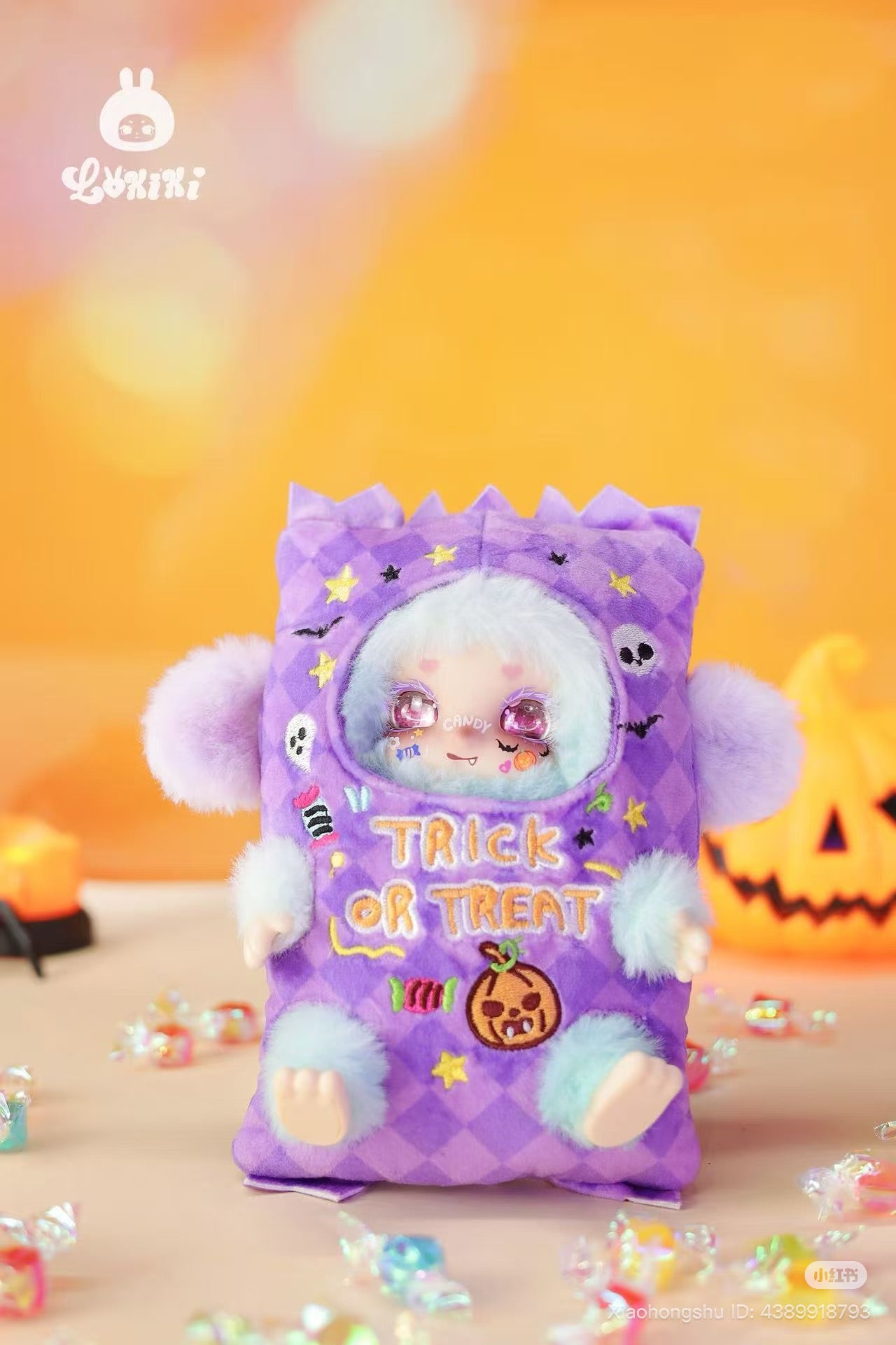 LOKKI Halloween Plush Blind Box Series doll in a purple costume with festive embroidery, surrounded by candies and a lit jack-o’-lantern backdrop.