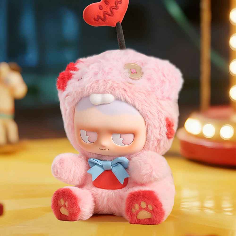 MONBOO-Monster Paradise Series Plush Blind Box toy, pink and fluffy with a heart antenna, blue bow, and cartoonish face, seated in a cozy setting.