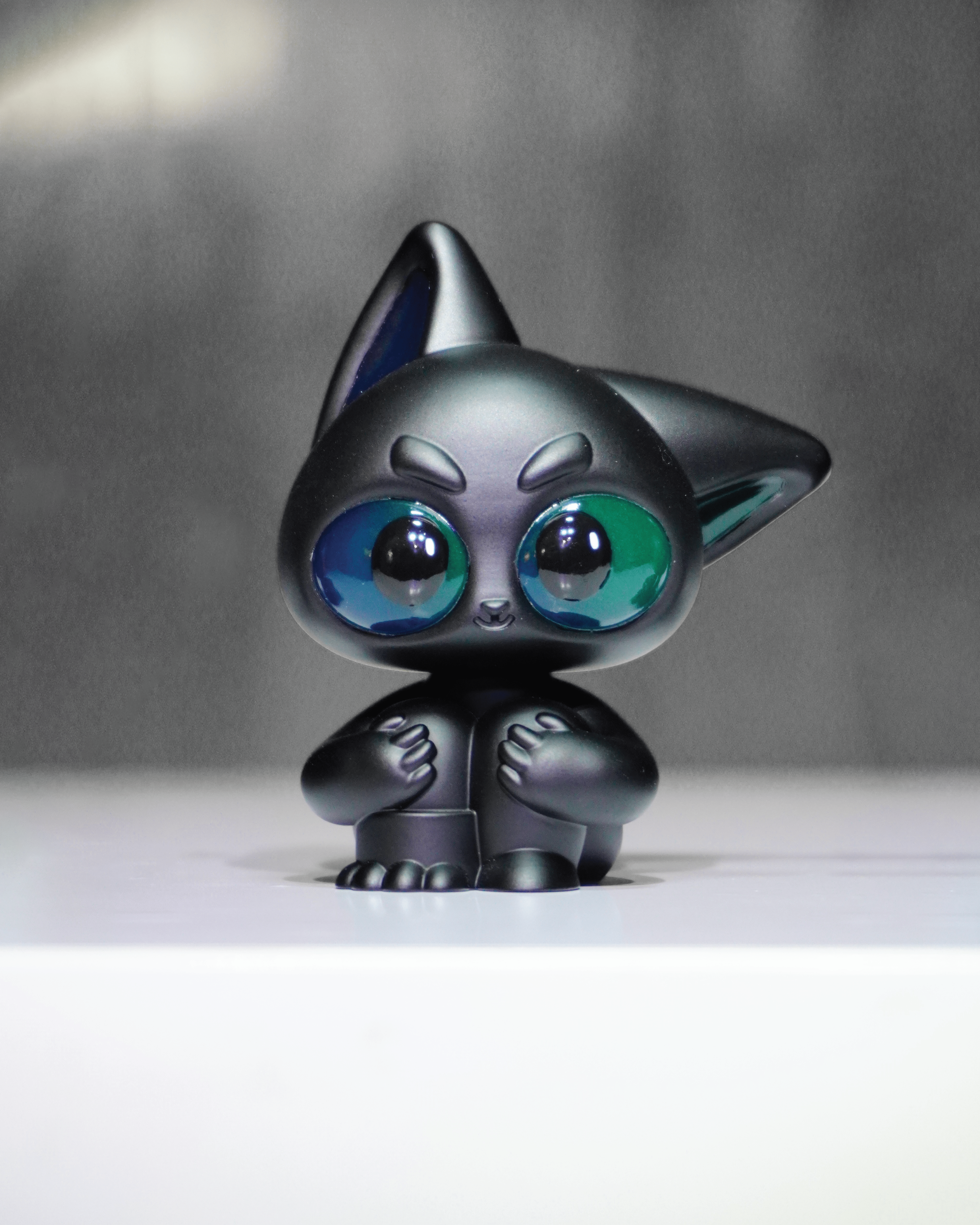 Noir by Wapu: A matte-black, stylized resin figurine with green-blue eyes, pointed ears, and small paws, embodying a cat or fox-like creature.