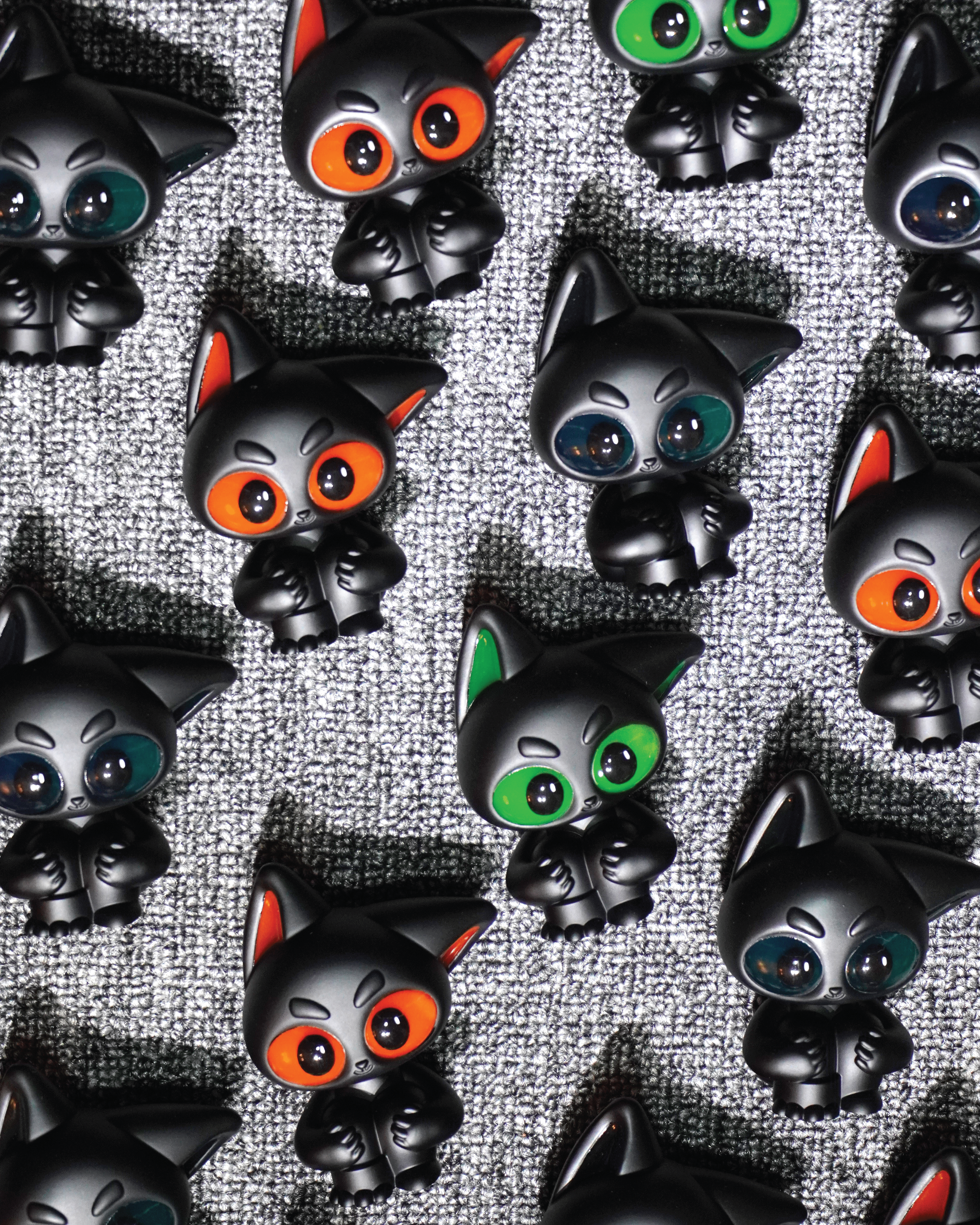 Noir by Wapu: Small black cat figurines with oversized eyes in varied colors, creating a vibrant, checkerboard effect. Each is 3 resin, embodying Strangecat Toys' artful charm.