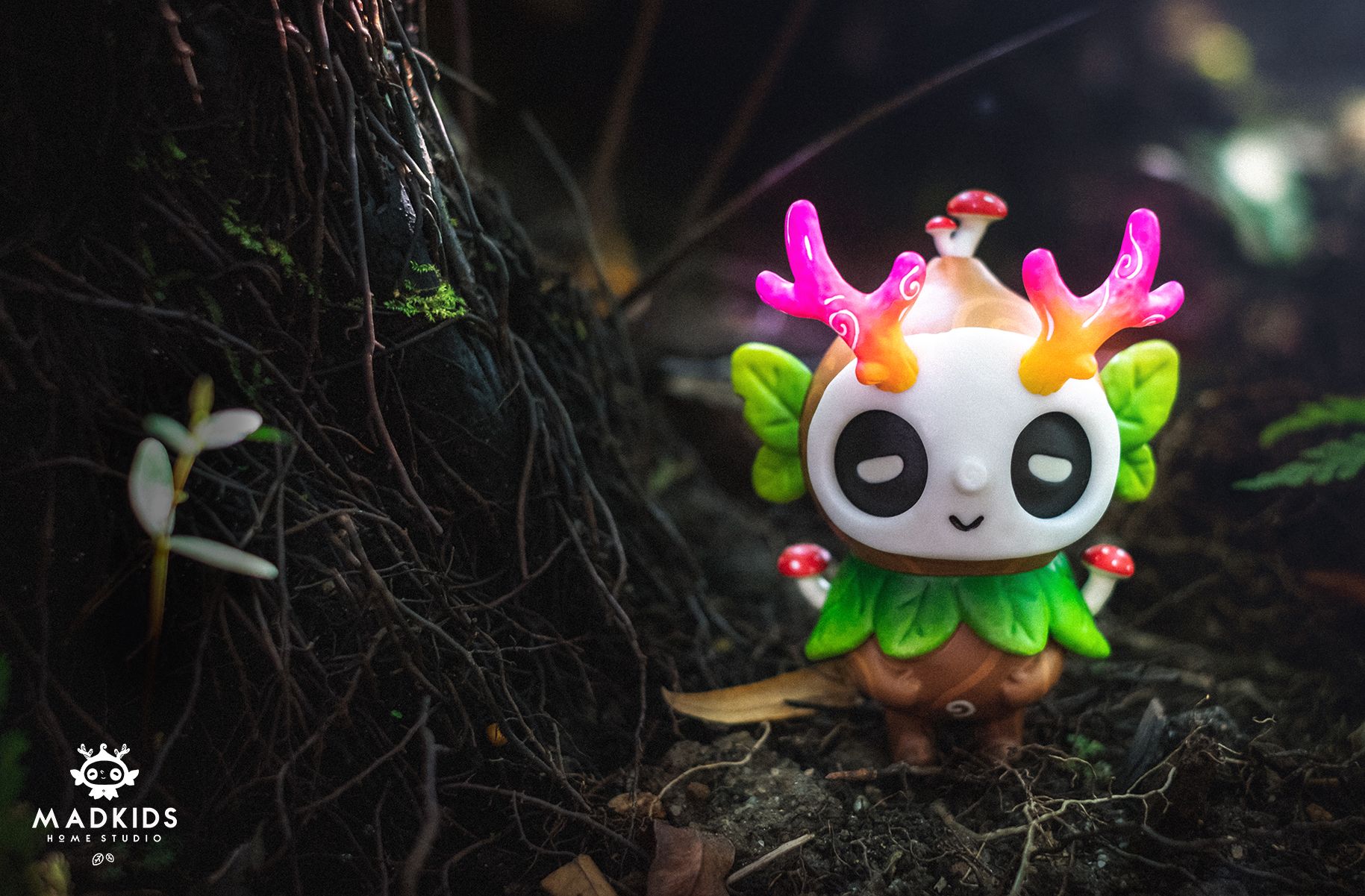 Ori Muffinn: The Wooden Brown vinyl toy with panda-like face, vibrant antlers, leaf wings, and tree-like body, staged on forest floor. Collectible art by Madkids.