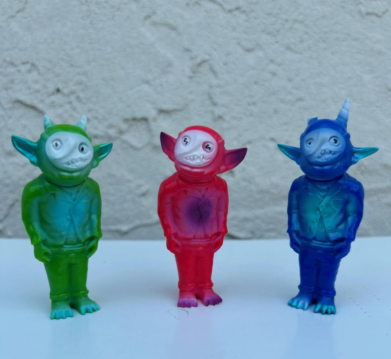 Goblins by Gloopy Goblin: Three small, translucent vinyl figurines with big ears and toothy grins, each uniquely colored, posed together on a white surface.