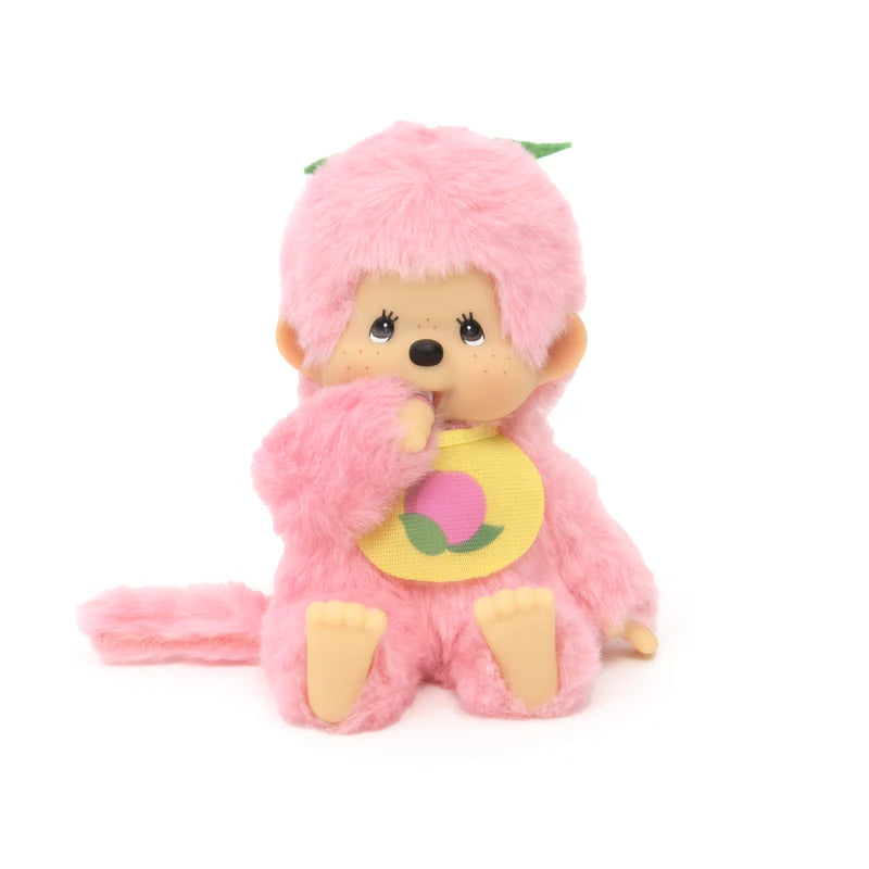 Monchhichi Fruit Beanies Plush, a 5.5 doll with fuzzy pink fur, sits upright with a thumb in its mouth, wearing a yellow bib featuring a peach.