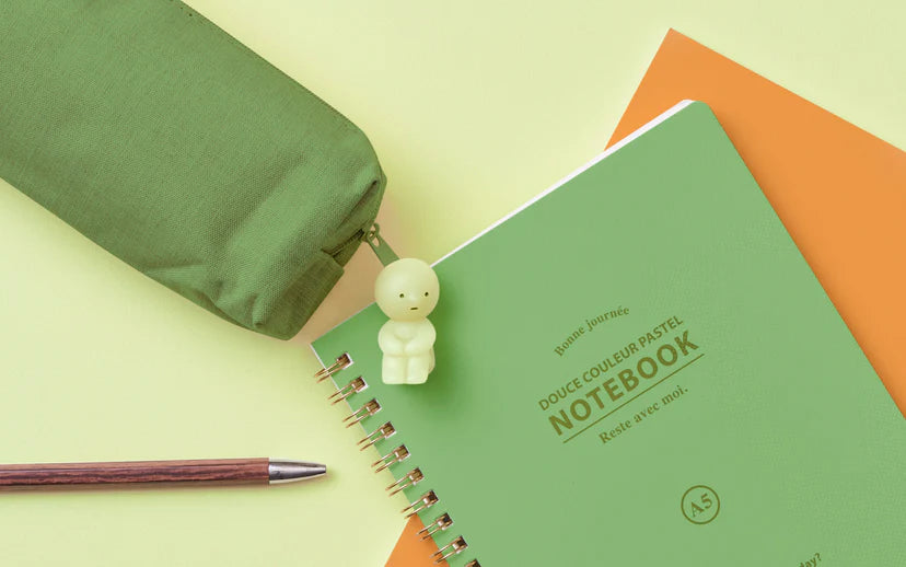 Smiski ZipperBites: A green notebook with a glowing Smiski toy on top.
