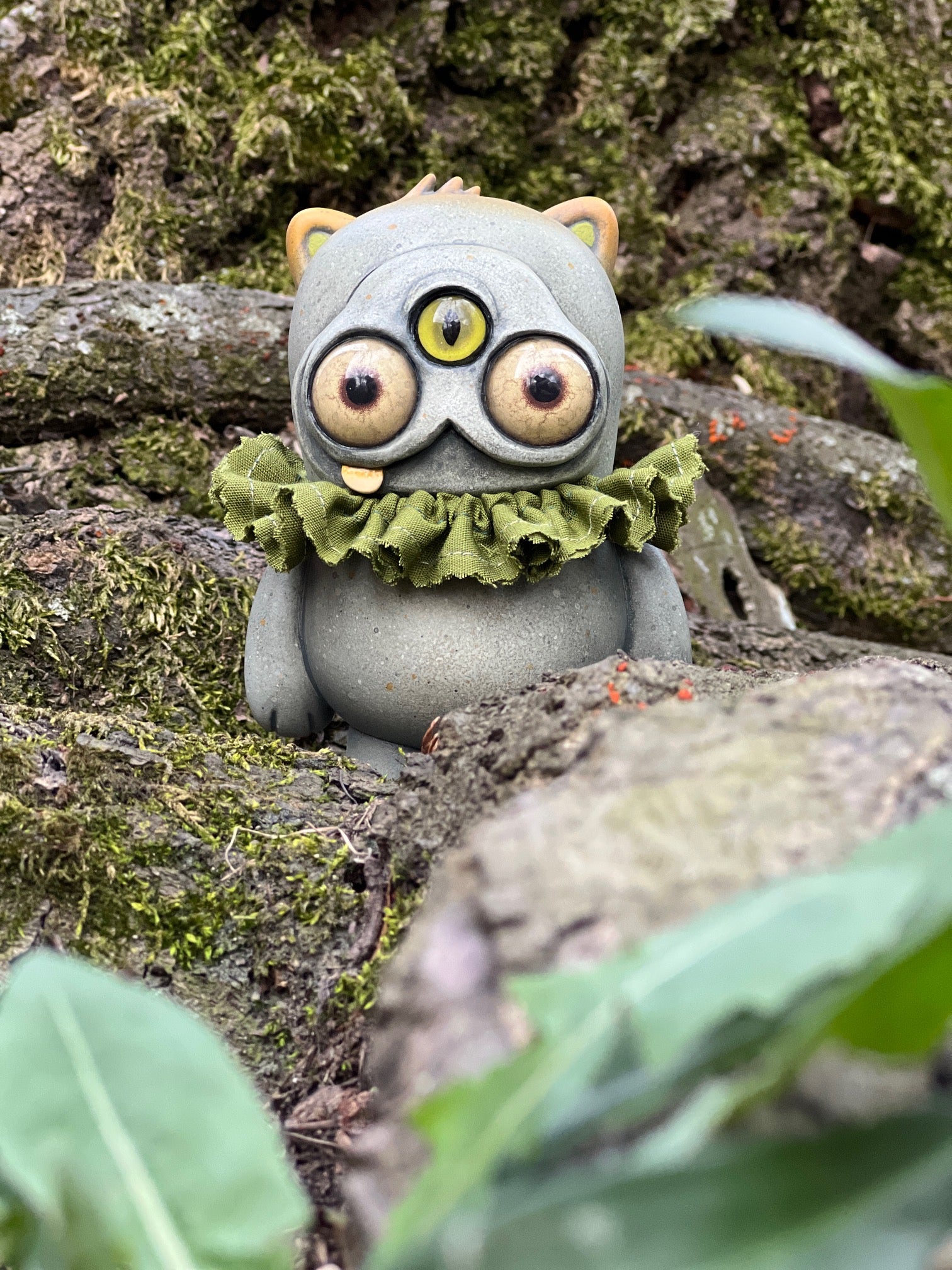 Ruffletoof Beans figurine: a 5 vinyl toy with three eyes, cat-like ears, and a ruffled collar, posed on a forest floor. Preorder for May 2026.